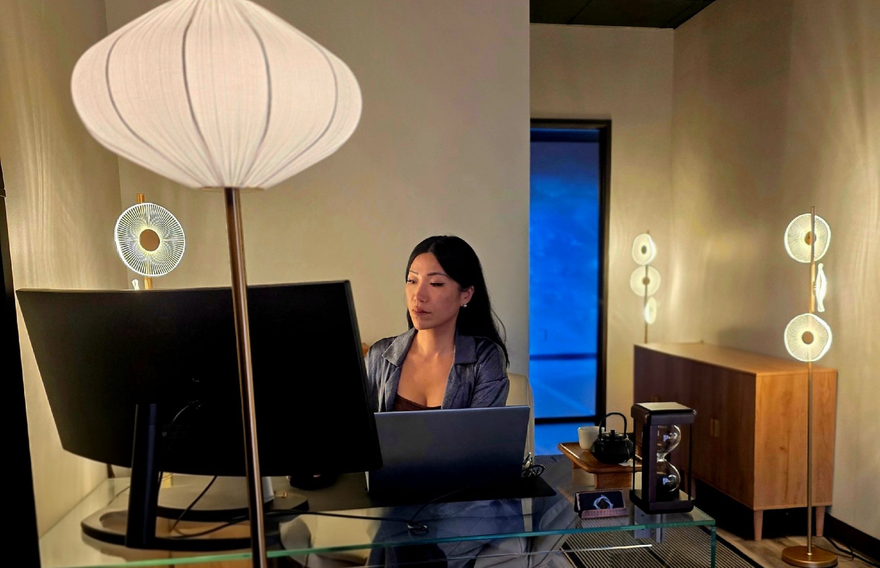 Everest Laina at her glass desk in the studio, Tacoma, with the blue window glowing behind her