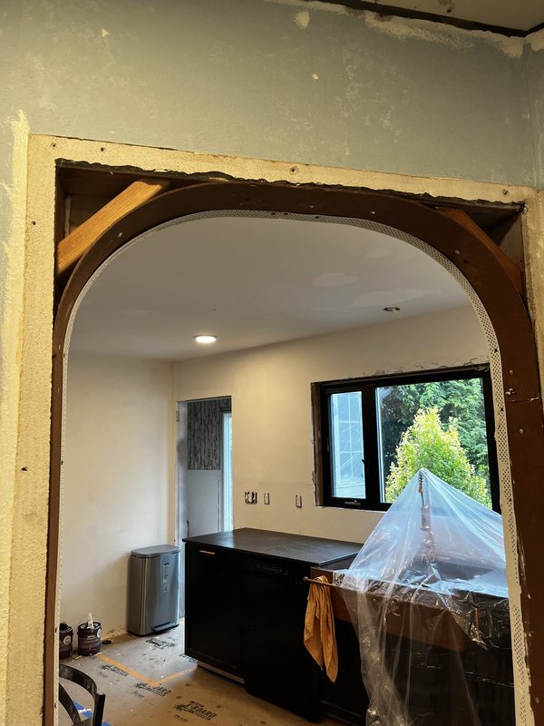 A rounded arch framed into a wall, with a kitchen and a window beyond it