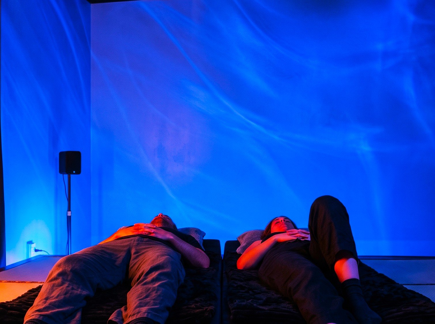 Two people resting on the vibroacoustic futons under moving blue light
